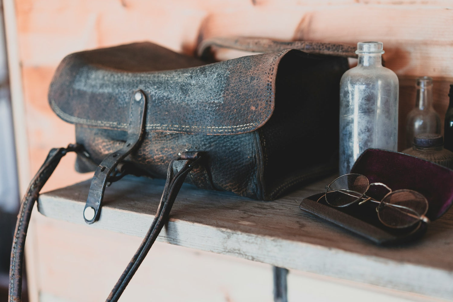 Alte Ledertasche mit weißem Schimmel auf Regal neben Glasflasche und Nikelbrille in Lederetui